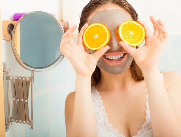 Mulher com máscara facial de lama detém fatia de laranja — Fotografia de Stock