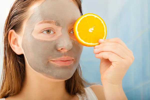 Mulher com máscara facial de lama detém fatia de laranja — Fotografia de Stock