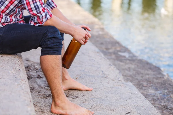 Man depressed with wine bottle sitting on beach outdoor — Stock Photo, Image