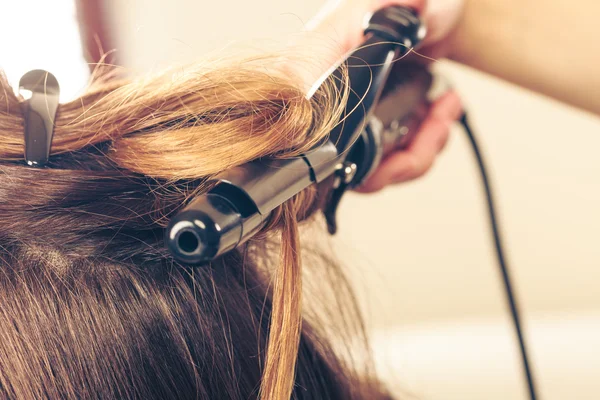 Estilista rizando el pelo para mujer joven. — Foto de Stock