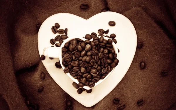 Heart shaped cup with coffee beans on brown — Stock Photo, Image