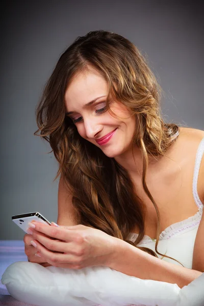 Mujer en la cama sosteniendo teléfono móvil. — Foto de Stock