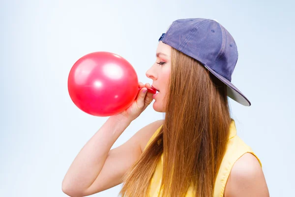 Menina em boné soprando balão vermelho . — Fotografia de Stock