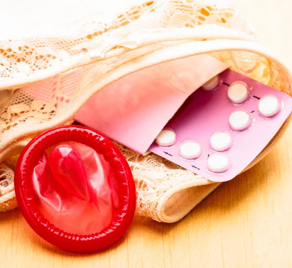 Oral contraceptive pills and condom on lace lingerie — Stock Photo, Image