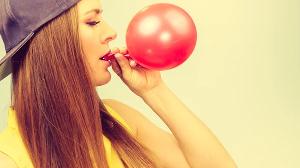 Kobieta w cap dmuchanie czerwony balon. — Zdjęcie stockowe