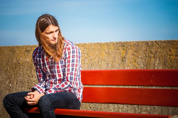 Man långt hår sitter på bänken utomhus — Stockfoto