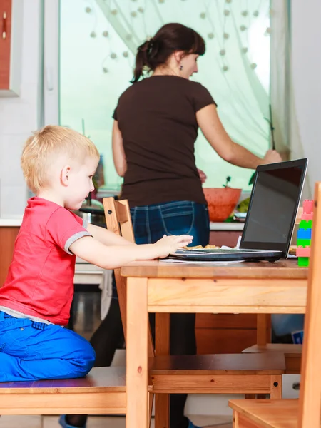 笔记本电脑和妈妈在打扫的小男孩 — 图库照片