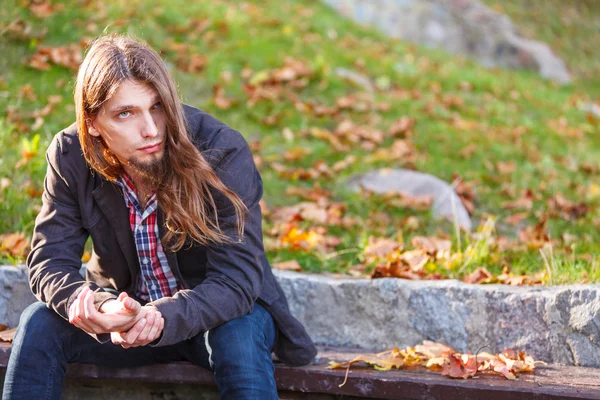 Homme cheveux longs assis sur le banc dans le parc d'automne — Photo