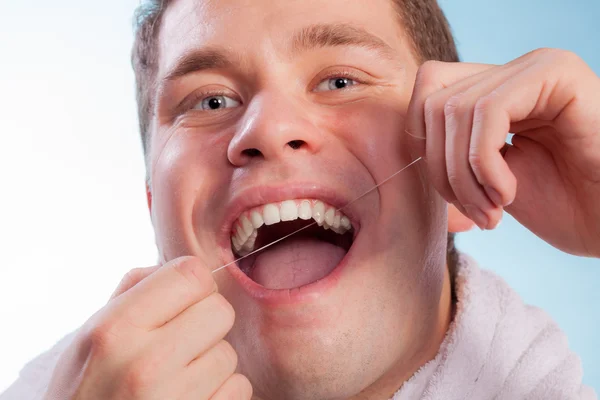 Ung mann som rengjør sine hvite tenner med tanntråd – stockfoto