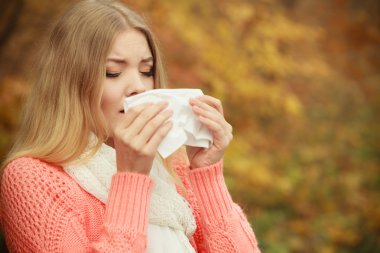 Sick ill woman in autumn park sneezing in tissue. clipart
