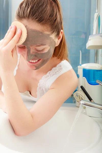 महिला बाथरूम में चेहरे की मिट्टी मिट्टी मास्क हटा रही है — स्टॉक फ़ोटो, इमेज