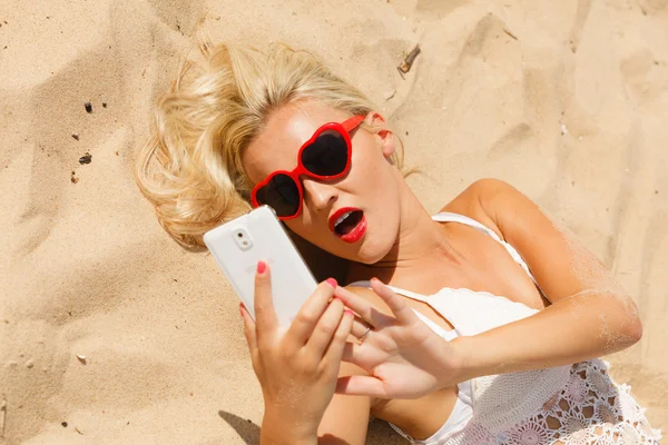 Woman lying on sandy beach using cell phone — Stock Photo, Image