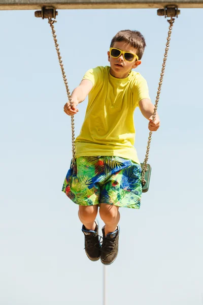 Boy playing swinging by swing-set. — Stock Photo, Image