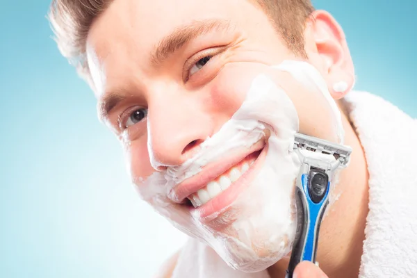 Happy man shaving using razor with cream foam.