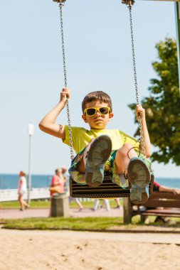 Boy playing swinging by swing-set. clipart