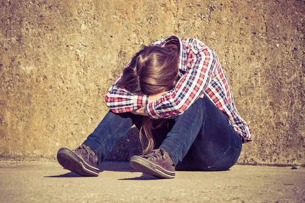 Mann mit langen Haaren sitzt traurig allein auf Grunge-Wand — Stockfoto