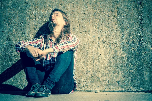 Hombre de pelo largo sentado solo triste en la pared grunge —  Fotos de Stock