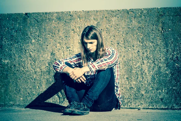 Homme aux cheveux longs assis seul triste sur le mur grunge — Photo