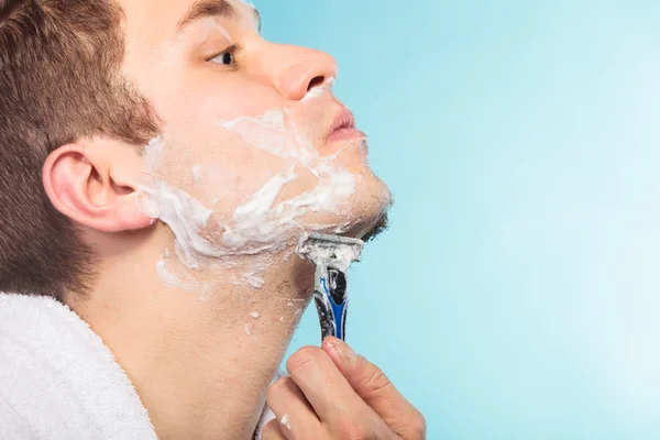 Jeune homme rasage à l'aide d'un rasoir avec mousse crème . — Photo