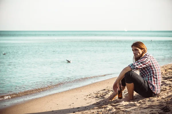 Mann sitzt deprimiert mit Weinflasche am Strand — Stockfoto