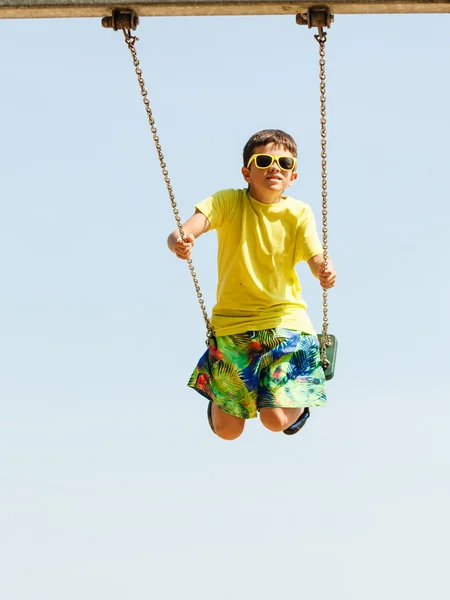Chłopiec gra swinging przez huśtawka zestaw. — Zdjęcie stockowe