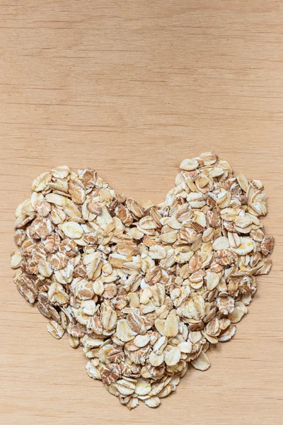 Oat flakes cereal heart shaped on wooden surface. — Stock Photo, Image