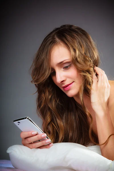 Mujer en la cama sosteniendo teléfono móvil. — Foto de Stock