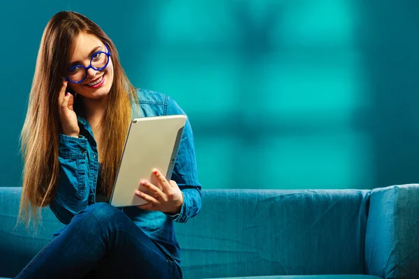 Nainen, jolla on tabletti istuu sohvalla sininen väri — kuvapankkivalokuva