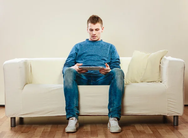 Jovem com tablet digital sentado no sofá — Fotografia de Stock