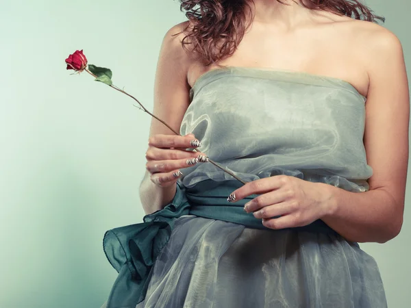Vrouw in groene jurk houden rode roos — Stockfoto