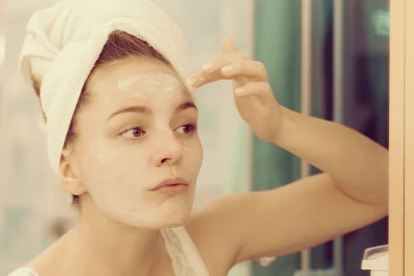 Mujer aplicando crema mascarilla en la cara en el baño —  Fotos de Stock