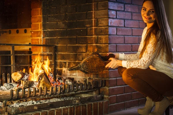 Woman at home fireplace making fire with bellows. — Stock Photo, Image