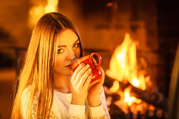 Woman drinking hot coffee relaxing at fireplace. — Stock Photo, Image