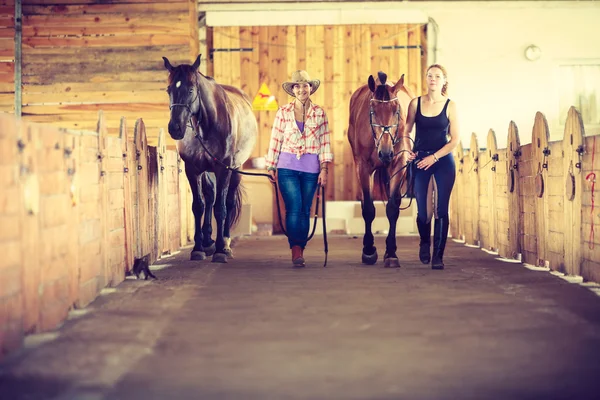 Cowgirl und junge Frau im Pferdestall. — Stockfoto