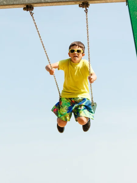 Boy playing swinging by swing-set. — Stock Photo, Image