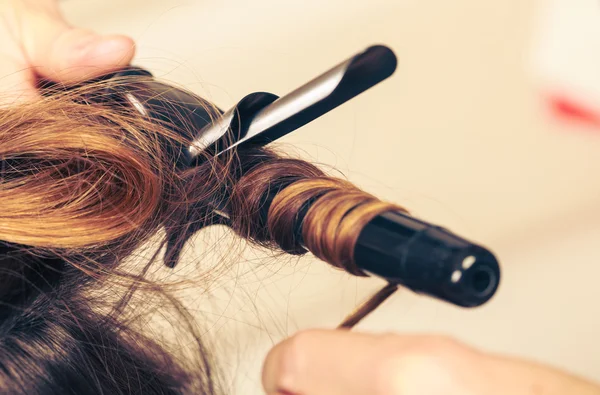 Stylist krullend haar voor jonge vrouw. — Stockfoto