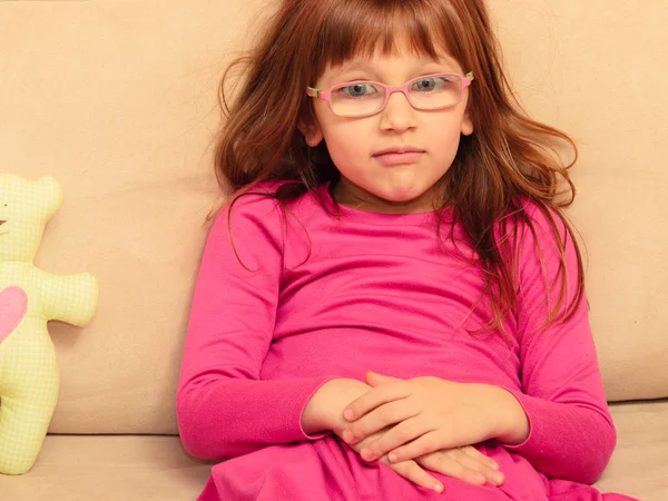 Triste niña pequeña sentada en el sofá con juguete — Foto de Stock