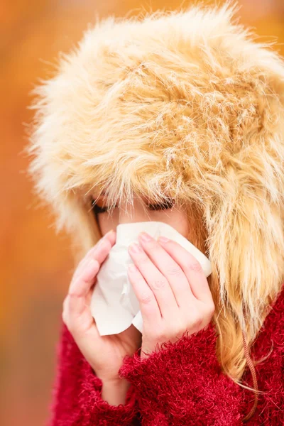 Sick woman in autumn park sneezing into tissue. — Stock fotografie