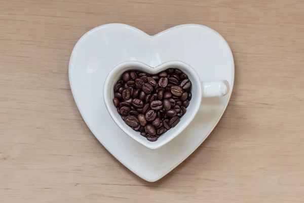 Herzförmige Tasse mit Kaffeebohnen auf Holztisch — Stockfoto