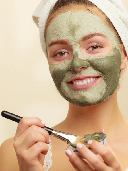 Woman applying with brush clay mud mask to her face