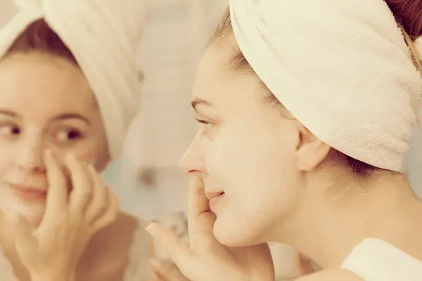 Mulher aplicando creme máscara no rosto no banheiro — Fotografia de Stock