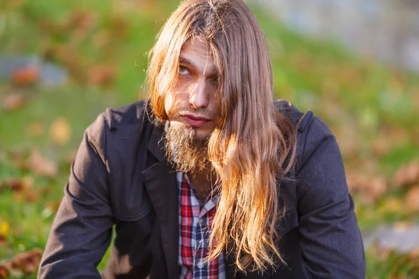 Man långt hår sitter på bänken i höst park — Stockfoto