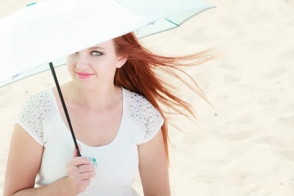 Redhaired girl sitting under umbrella on beach. — Stock Photo, Image