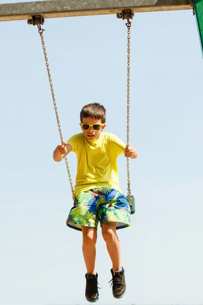 Boy playing swinging by swing-set. — Stock Photo, Image