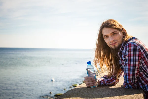 Hombre pelo largo relajante por la playa agua potable — Foto de Stock