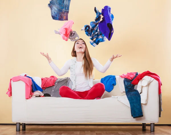 Ευτυχισμένη γυναίκα στον καναπέ σε βρώμικο δωμάτιο ρίχνοντας ρούχα — Φωτογραφία Αρχείου