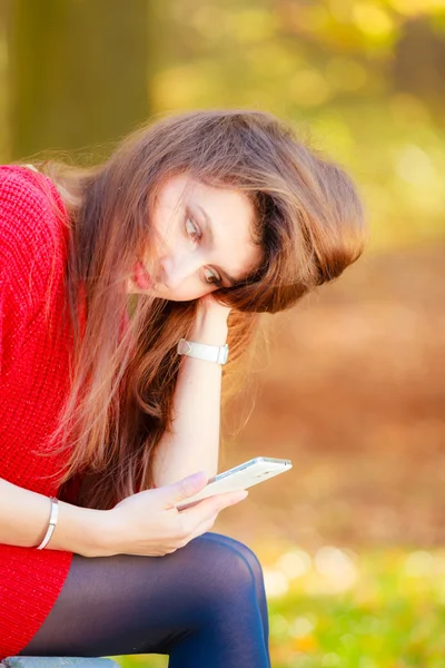 Treurige vrouw in park met telefoon. — Stockfoto