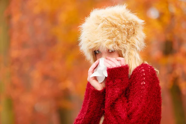 Sick woman in autumn park sneezing into tissue. — 图库照片