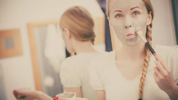 面部干性皮肤和身体护理 在家里处理皮肤的概念 年轻女子用毛刷在脸上涂上灰泥面罩 露出滑稽的表情 — 图库照片