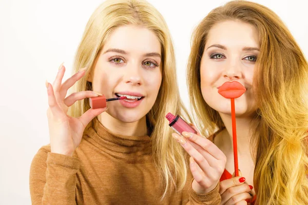 两个女人一边化妆一边玩乐 朋友们手握唇彩或口红 假唇涂在唇膏上 — 图库照片
